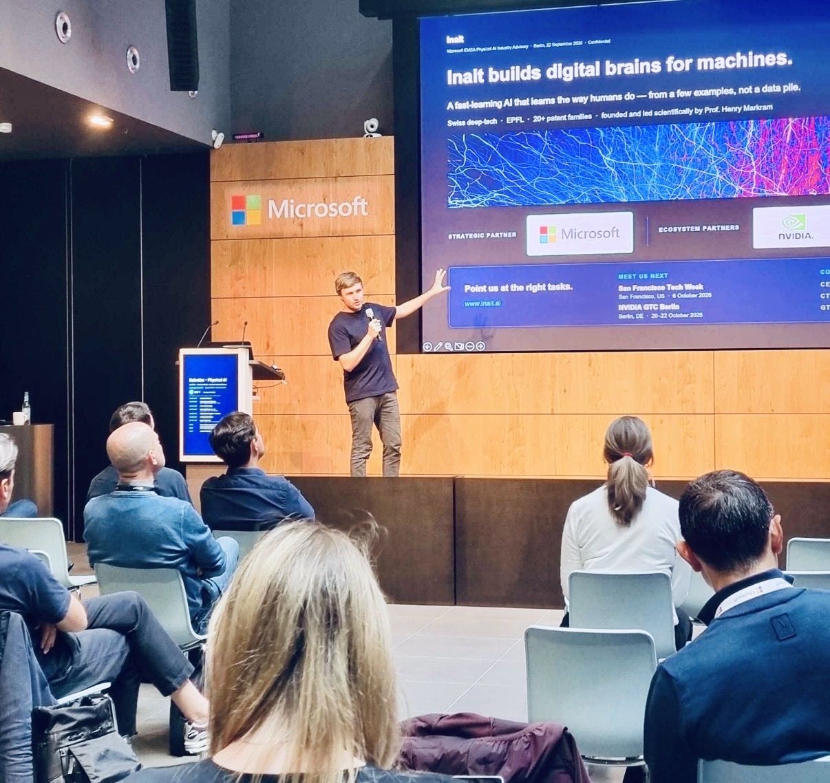 Daniel Lütgehetmann on stage at Microsoft Berlin, presenting the slide "Inait builds digital brains for machines" to an audience